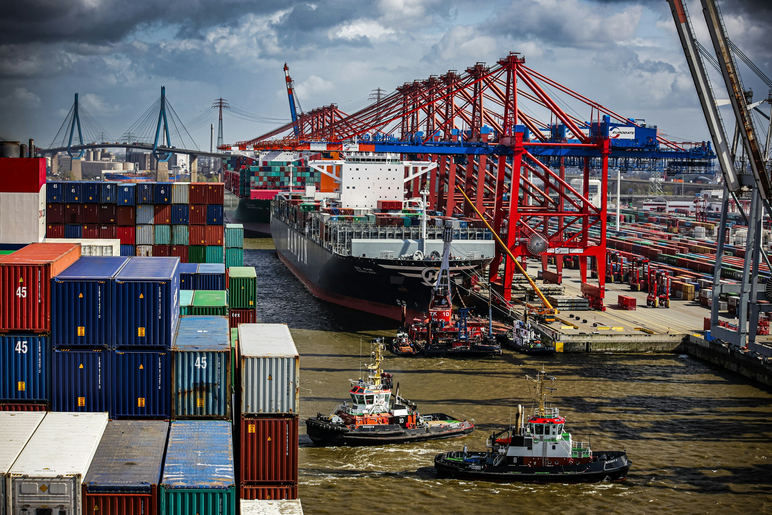 Container vessel at a port terminal with cranes and tugboats